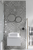 Modern white sink with floating base unit on section of wall with ornate grey tiles