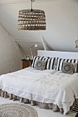 Double bed with pillows against headboard below pendant lamp with basketwork lampshade