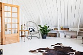 Cowhide rug on white floor in attic room with wood-clad sloping ceiling, shelves on knee wall and open interior door