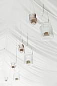 Festive arrangement of candle lanterns hung from white tent ceiling for wedding