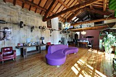Curved purple sofa on wooden floor in converted loft apartment with wooden roof structure and gallery