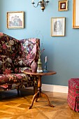 Biedermeier table next to floral armchair and blue wall