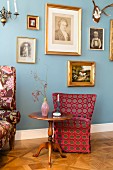 Biedermeier table in front of spotted armchair and blue wall