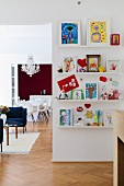 Colourful children's drawings on white floating shelves in open-plan interior