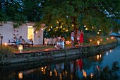 Romantische Gartenparty am Abend mit Gästen zwischen Fackelleuchten und Lampions an Baumzweigen