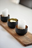 Candles in metal bowls on wooden board