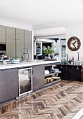 Modern kitchen island with glass door and integrated corner shelf on rustic herringbone parquet, in the background on the wall a vintage station clock
