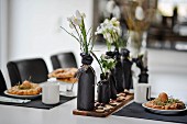 Gedeckter, weisser Ostertisch mit in schwarzem Papier gewickelten Flaschen als Blumenvasen und schwarzen Tischsets