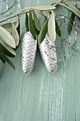 Pine cones covered in silver foil and lametta hanging from olive branch