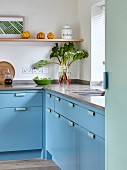 Pale blue, L-shaped kitchen counter with stone worksurface