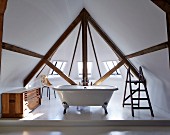 Free-standing bathtub in window bay in attic interior with exposed beams
