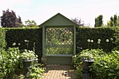 Small arbour with diagonal trellis and tall box hedges bordering summer garden