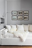 Cushions and sheepskin blanket on white couch below pictures on wall