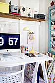 White desk with computer screen and rustic wall board next to light blue vintage window sash as pin board