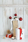 Gifts wrapped in red and white, baubles and angel made from log against board wall
