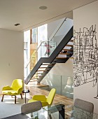 Modern staircase with glass balustrade and two yellow armchairs in contemporary interior