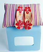 Flip-flops with red floral pattern and colourful striped cushion on pale blue stool