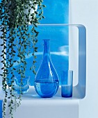 Rounded carafe and blue drinking glasses on metal shelf below trailing succulent