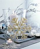 Christmas arrangement of white candles in various glass vessels and snowflake ornament