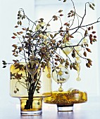 Branches of rose hips decorated with glass baubles in yellow glass vase