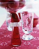 Bottle of Campari and soda decorated with Father Christmas hat on red table runner next to glass with etched initial