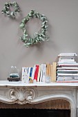 Two wreaths of dried leaves above books on mantelpiece of open fireplace