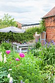 Blooming cottage garden with seating area next to brick barn