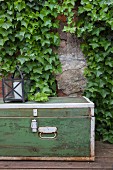 Old trunk and lantern in front of ivy-covered wall