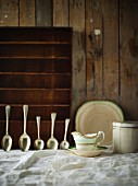 Sauce boat and silver spoons on white tablecloth against wooden wall
