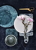 Green marble boards, ceramic dish and branches of flowering magnolia on marble board with leather strap