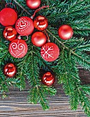 Red Christmas-tree baubles with hand-painted motifs on fir branch