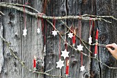 DIY-Sterne aus Modelliermasse und rote Christbaumkerzen am Ast vor Bretterwand