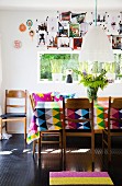 Colourful, geometric tablecloth on dining table, retro wooden chairs and collage of photos on wall above window