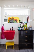 Rotes Waschbecken und schwarze Schubladenkommode vor Wand mit Spiegel
