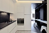 Breakfast bar and stools against dark wall in doorway leading from white minimalist designer kitchen