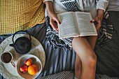 Woman lying on bed reading next to tray of tea and fruit