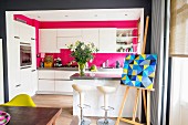 Open-plan kitchen with white, modern furnishings and hot pink walls