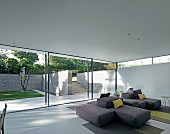 Loungebereich mit Designer-Sofalandschaft, Fensterfront und Blick auf sommerliche Terrasse mit Natursteinmauer