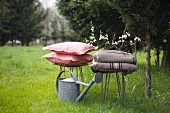Woollen blankets, zinc watering can and cushions on stools on lawn