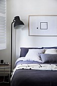 Schlafzimmer mit schwarzer Stehleuchte neben Bett, darüber gerahmtes Bild mit geometrischen Formen