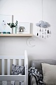 Children's room with white crib and gray armchair, storage and mobile with cloud motif above