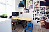 Dining and working area with yellow table, blue step-stool and collection of photos and framed posters on wall