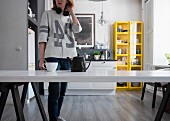 Woman wearing headphones standing next to teapot and teacup on kitchen table