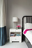 White bedside cabinet next to two-tone curtain
