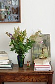 Vase of wildflowers and oak leaves next to stack of books