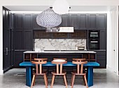 Custom-made kitchen with dining area, solid wooden chairs around blue-painted table opposite kitchen counter between dark fitted wardrobes