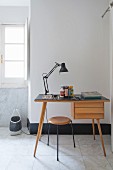 Desk lamp on desk and retro-style stool on marble-tiled floor