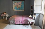 Table lamp on white chair next to bed with ethnic bedspread and map decorating wall in bedroom