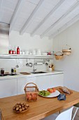 Walnuts and fresh fruit on wooden table in front of white kitchen counter below white wood-beamed ceiling