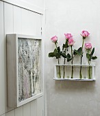 Roses in test tubes in wall bracket next to artwork